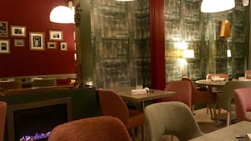 Ein Restaurantinneres mit Kamin, gerahmten Bildern an der Wand und modernen Leuchten.