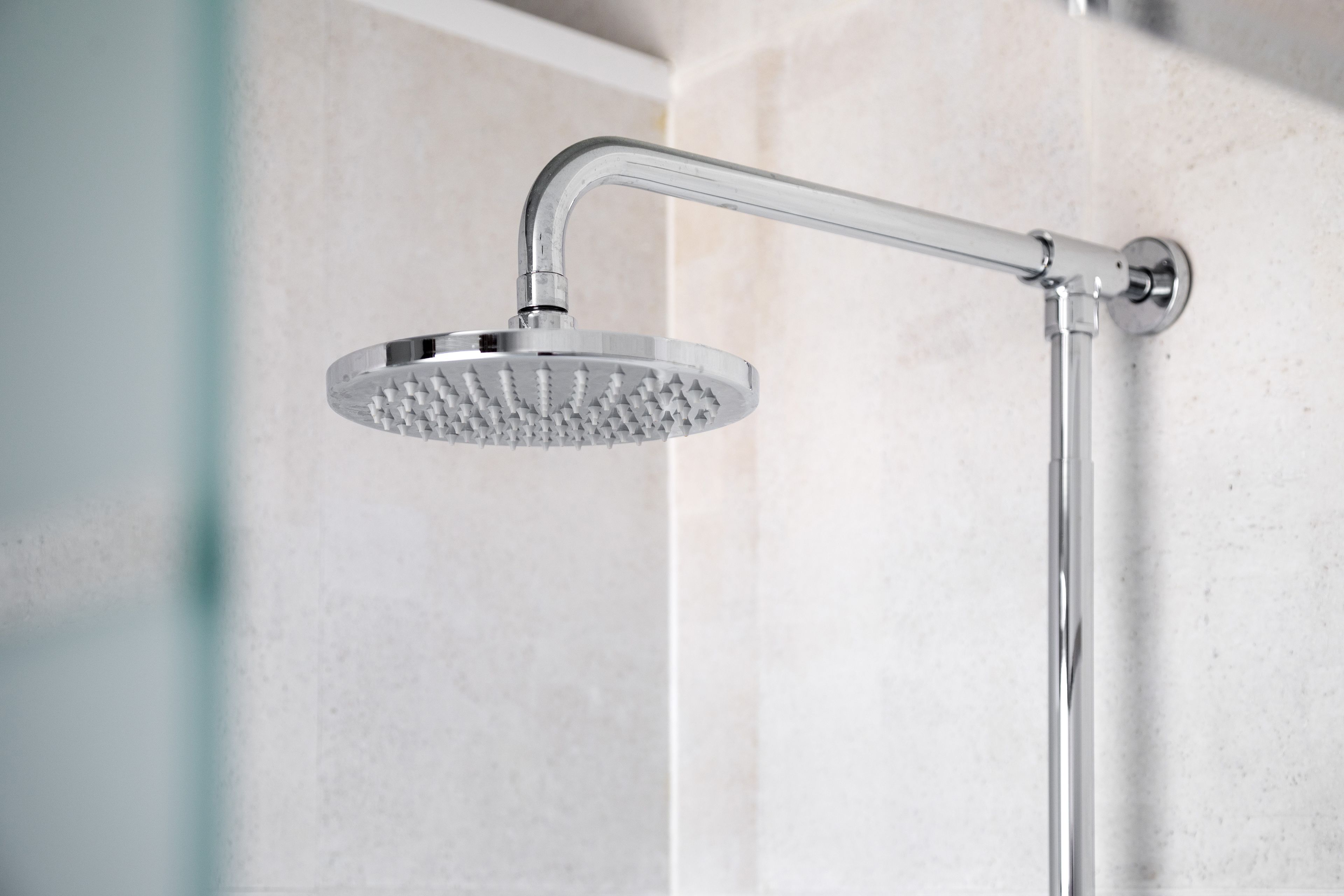 Une pomme de douche moderne au design incurvé, fixée au mur sur une surface recouverte de carreaux.