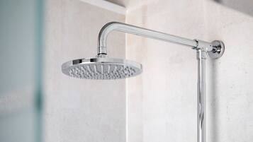 Une pomme de douche moderne au design incurvé, fixée au mur sur une surface recouverte de carreaux.