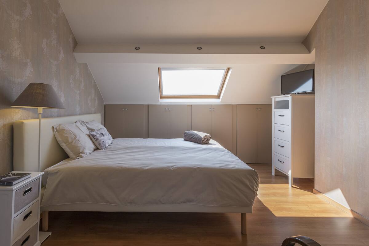 A bedroom with a skylight, a bed, a nightstand, a dresser, and a TV.