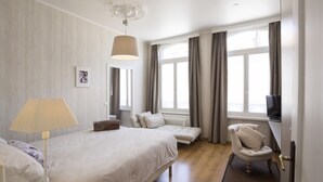 Hotellihuone, jossa on sänky, yöpöytälamppu, tuoli ja televisio.