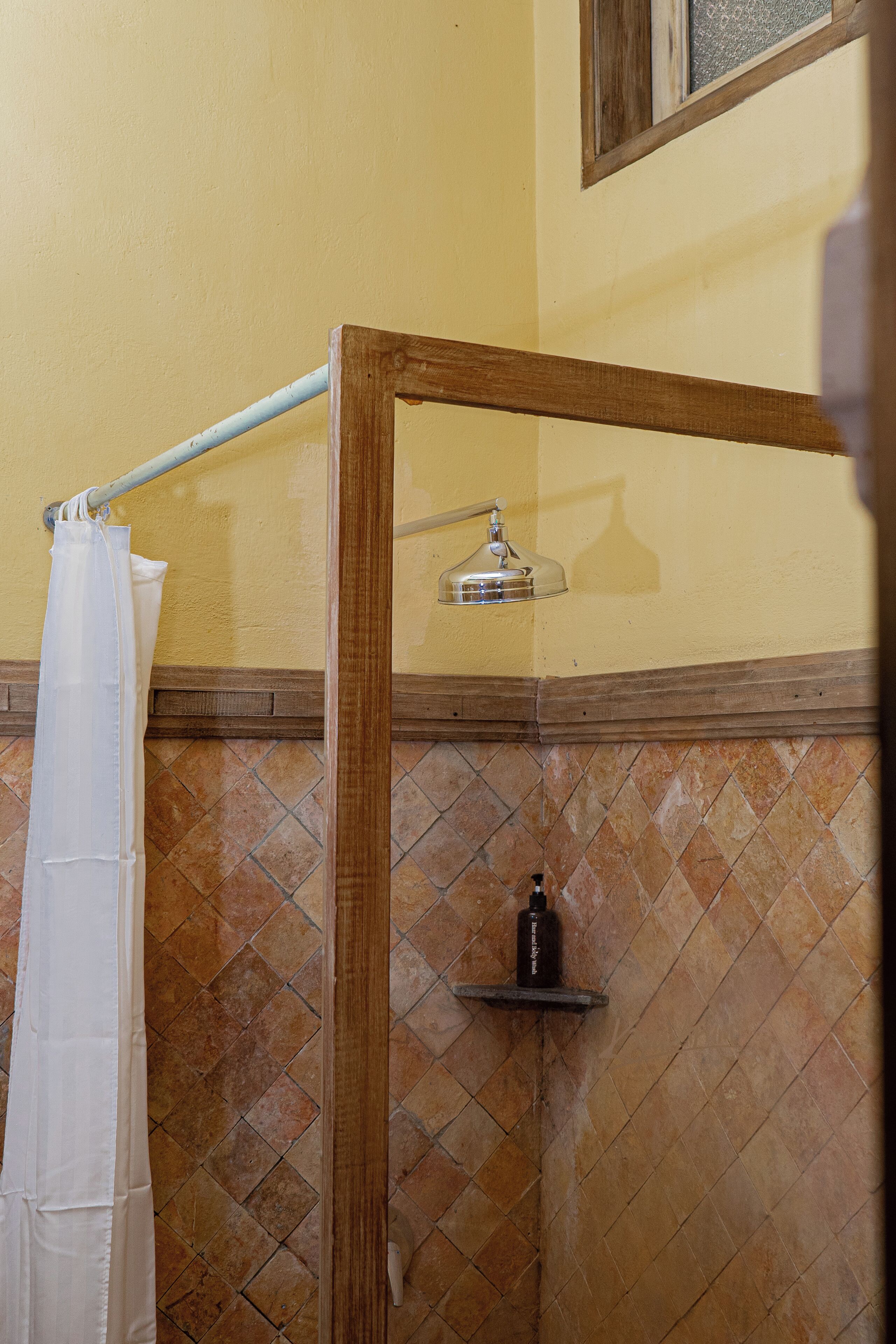 A shower area with a wooden frame, a white shower curtain, and a tiled wall.