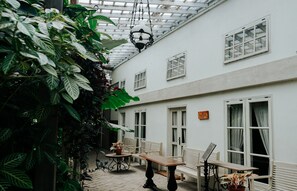 A covered outdoor area with a wooden table and benches, surrounded by potted plants and white-framed windows. - Kayu Arum Resort (Salatiga)