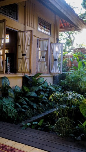 A traditional house with open windows and a lush garden. - Kayu Arum Resort (Salatiga)