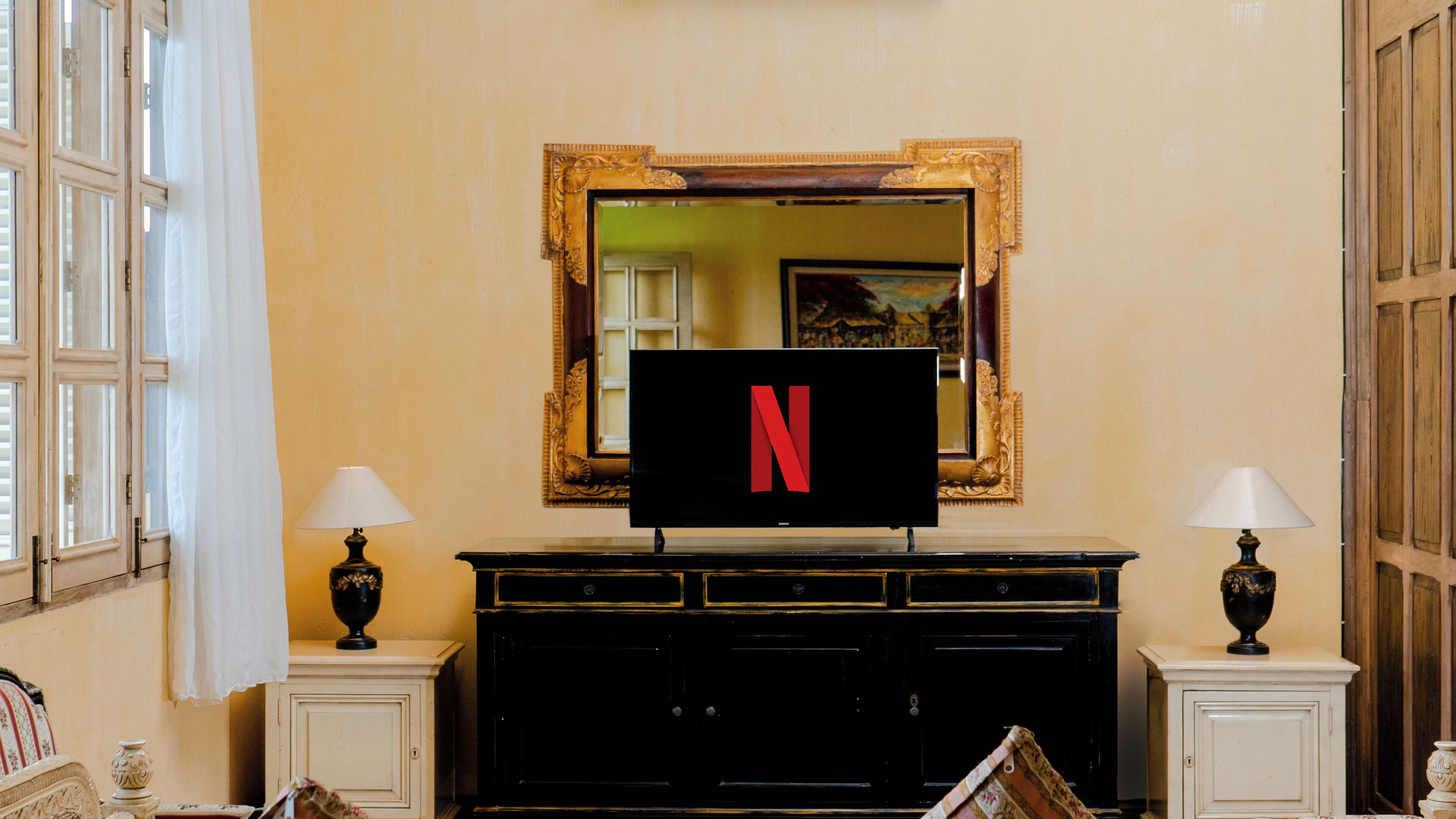 A room with a large black cabinet, two wall-mounted lamps, a mirror with a gold frame, and a television displaying the Netflix logo.