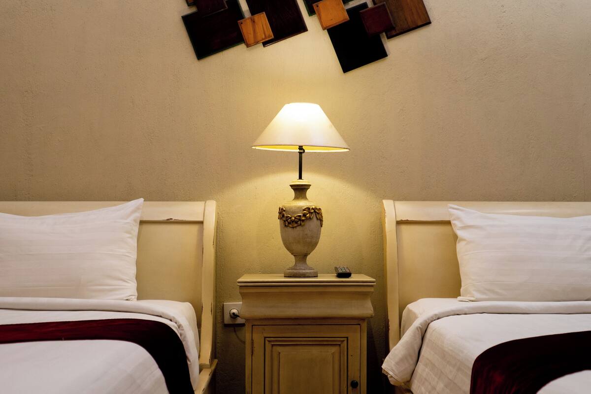 Ett hotellrum med två sängar, ett nattduksbord med en lampa och ett litet skåp.