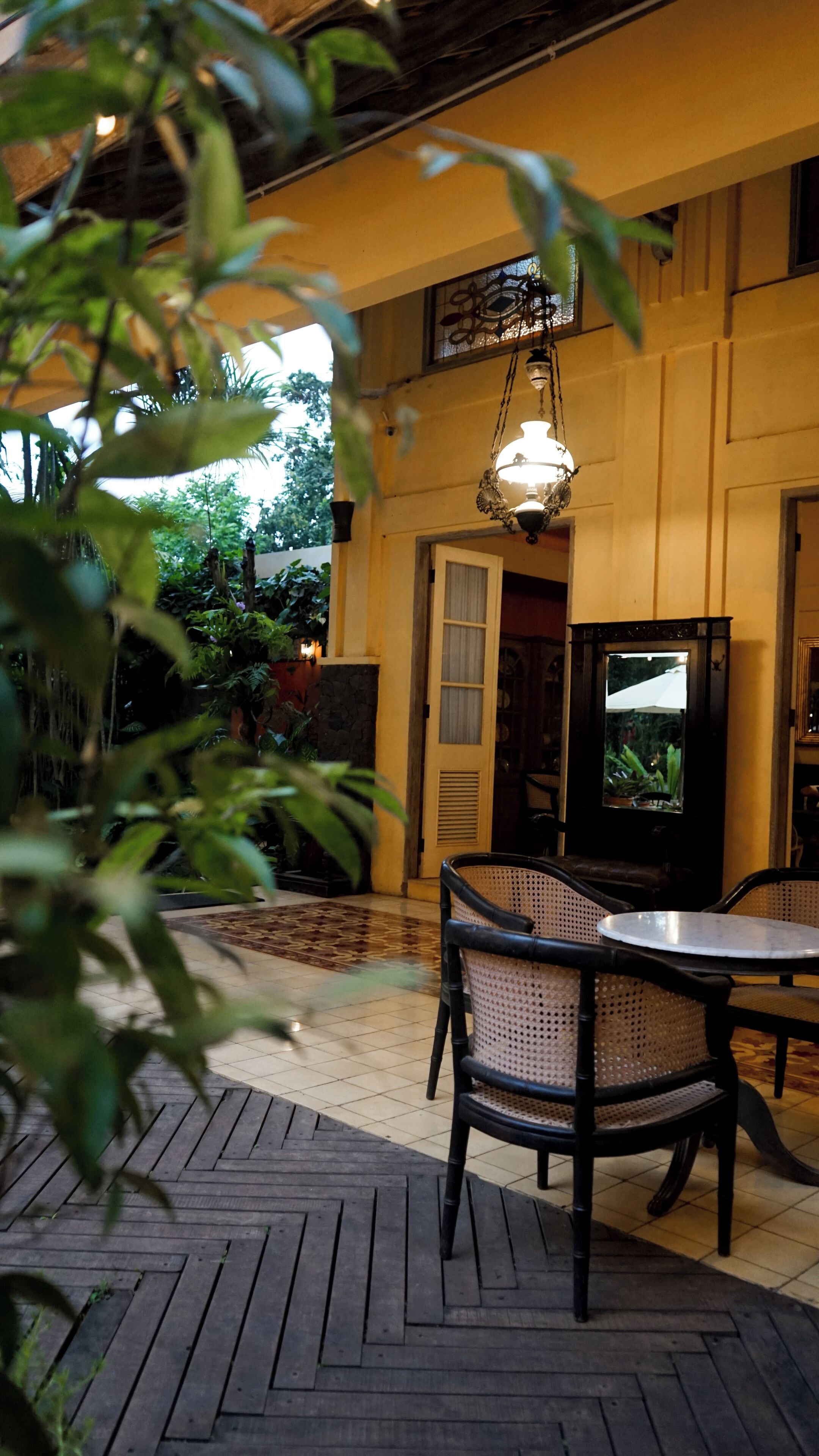 An outdoor patio with a table and chairs, a hanging light fixture, and a view of the garden.