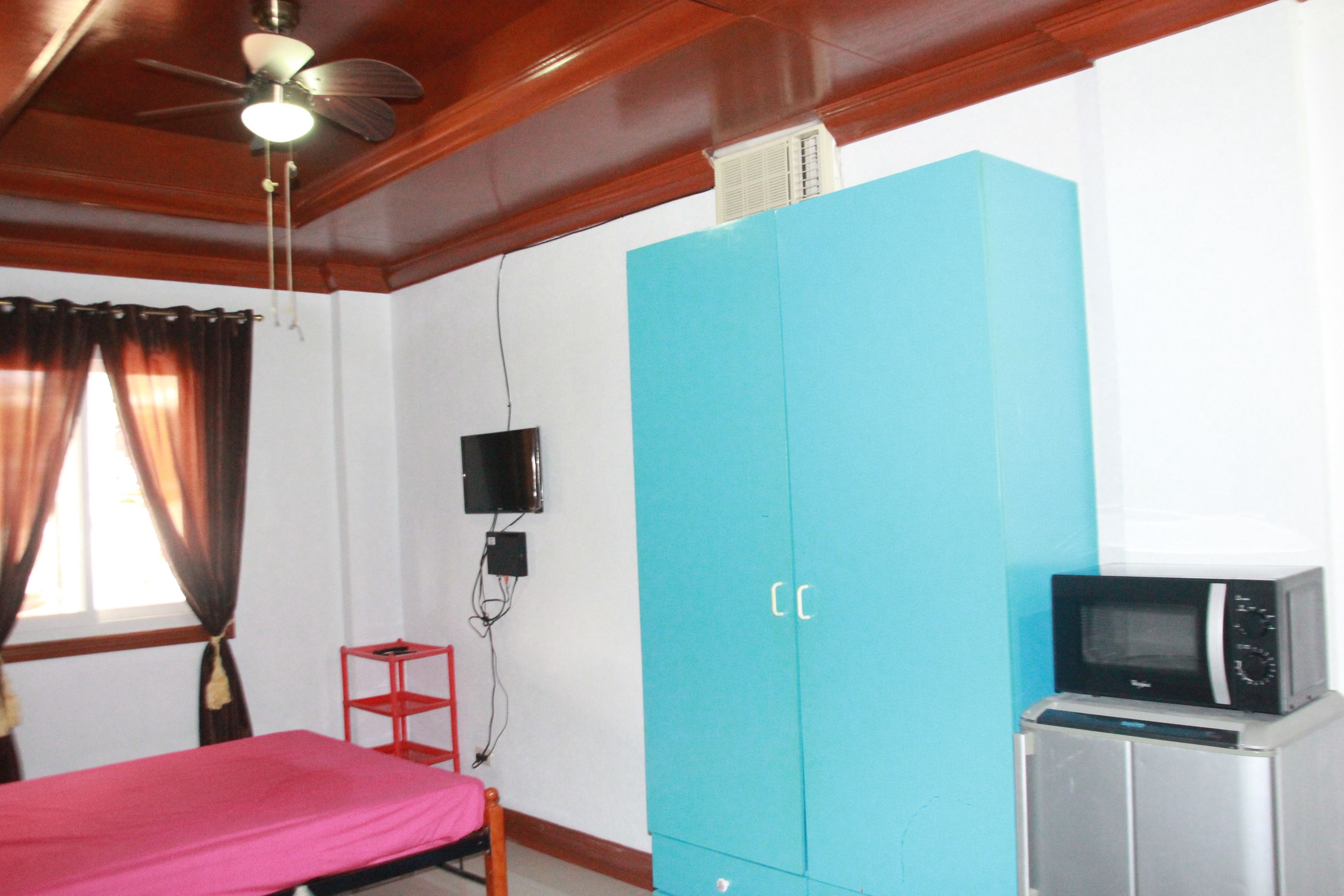 Une chambre avec un lit, une armoire bleue, une télévision et un four à micro-ondes.