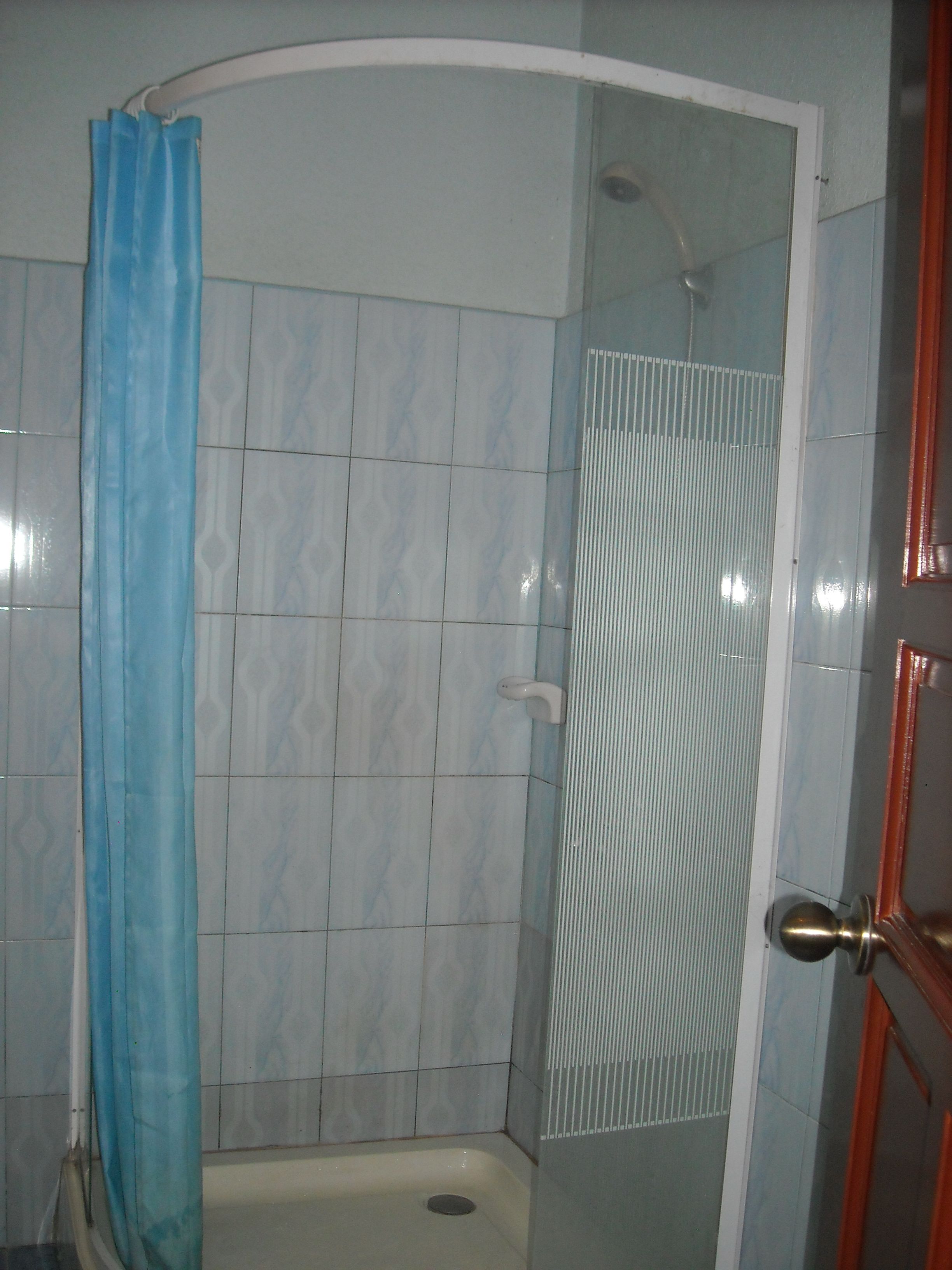 A bathroom with a shower, tiled walls, and a door with a brass handle.