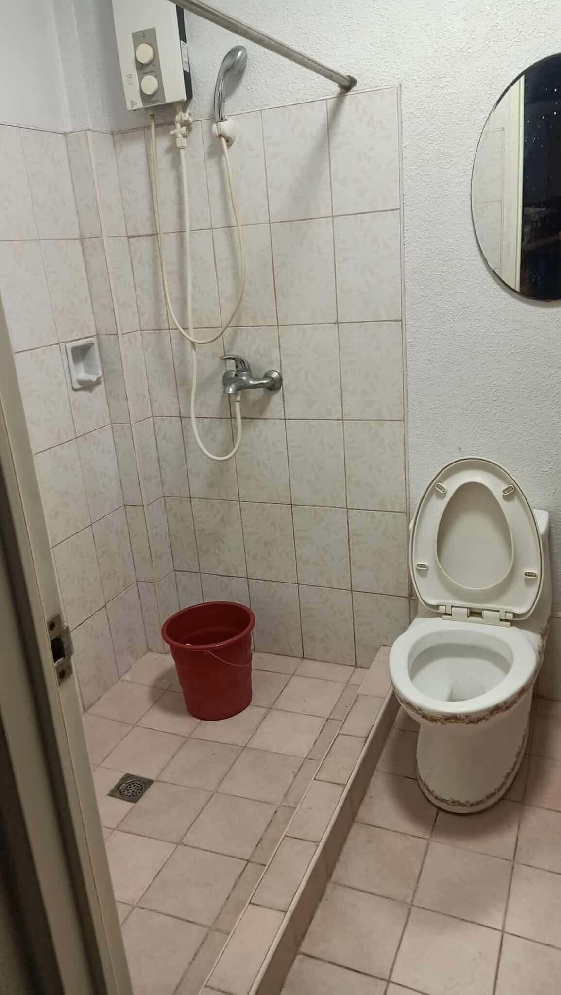 A small bathroom with a toilet, a shower, and a red bucket.