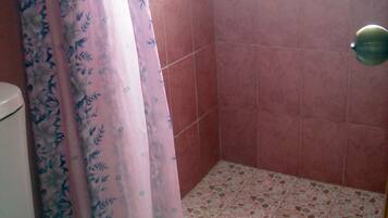 Un baño con inodoro, ducha con azulejos rosas y cortina de ducha con estampado floral.