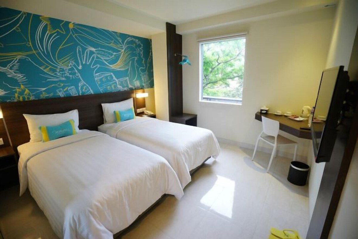 A hotel room with two beds, a desk, a chair, a large window, and a wall mural.