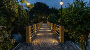 A paved pathway with railings and street lamps, surrounded by greenery and a body of water. - Amethyst Resort Passikudah (Pasikuda)