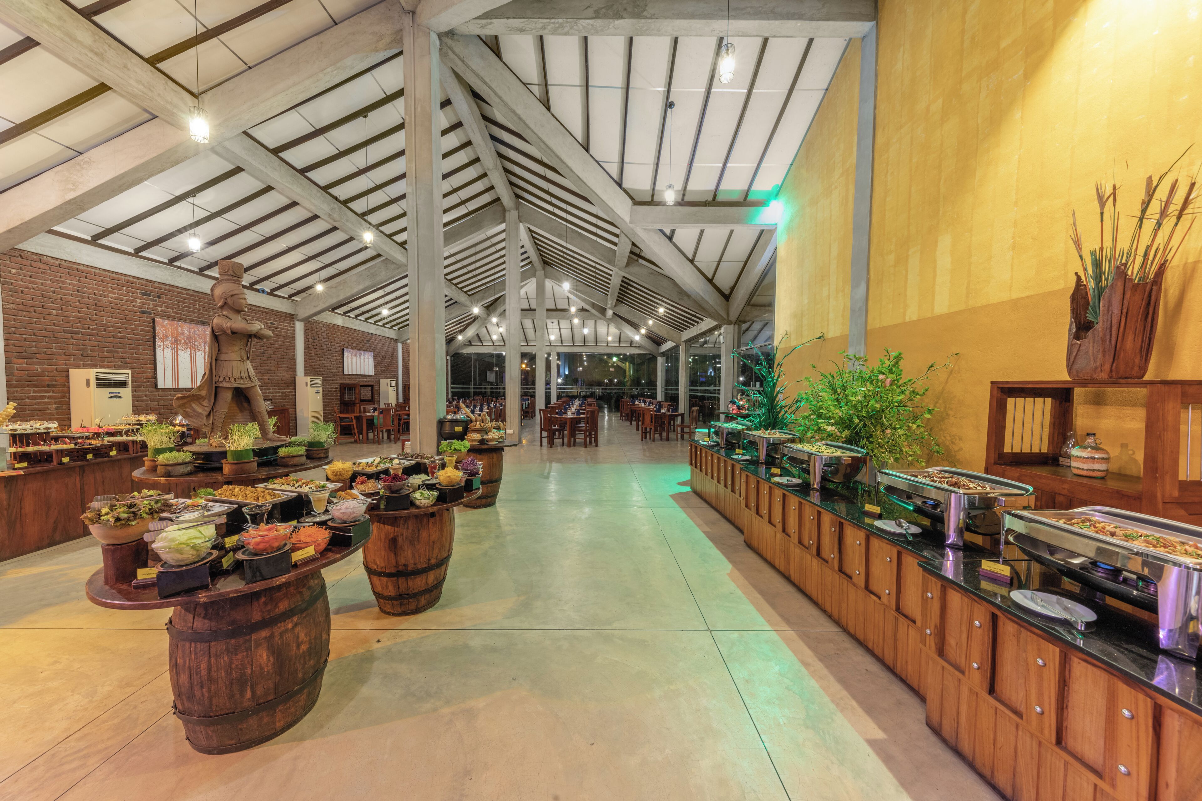 A spacious indoor area with a high ceiling, wooden barrels with food items, and a long counter with various dishes.