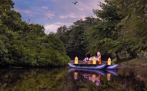A boat with two people and a table, surrounded by dense greenery and calm water.