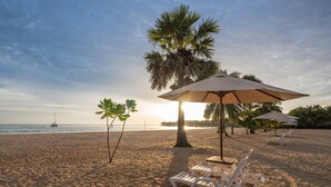 A beach with white lounge chairs and umbrellas, a palm tree, and a sunset over the ocean. - Amethyst Resort Passikudah (Pasikuda)