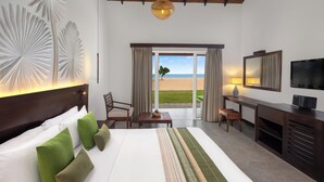 A hotel room with a large bed, a desk, a TV, and a view of the beach. - Amethyst Resort Passikudah (Pasikuda)