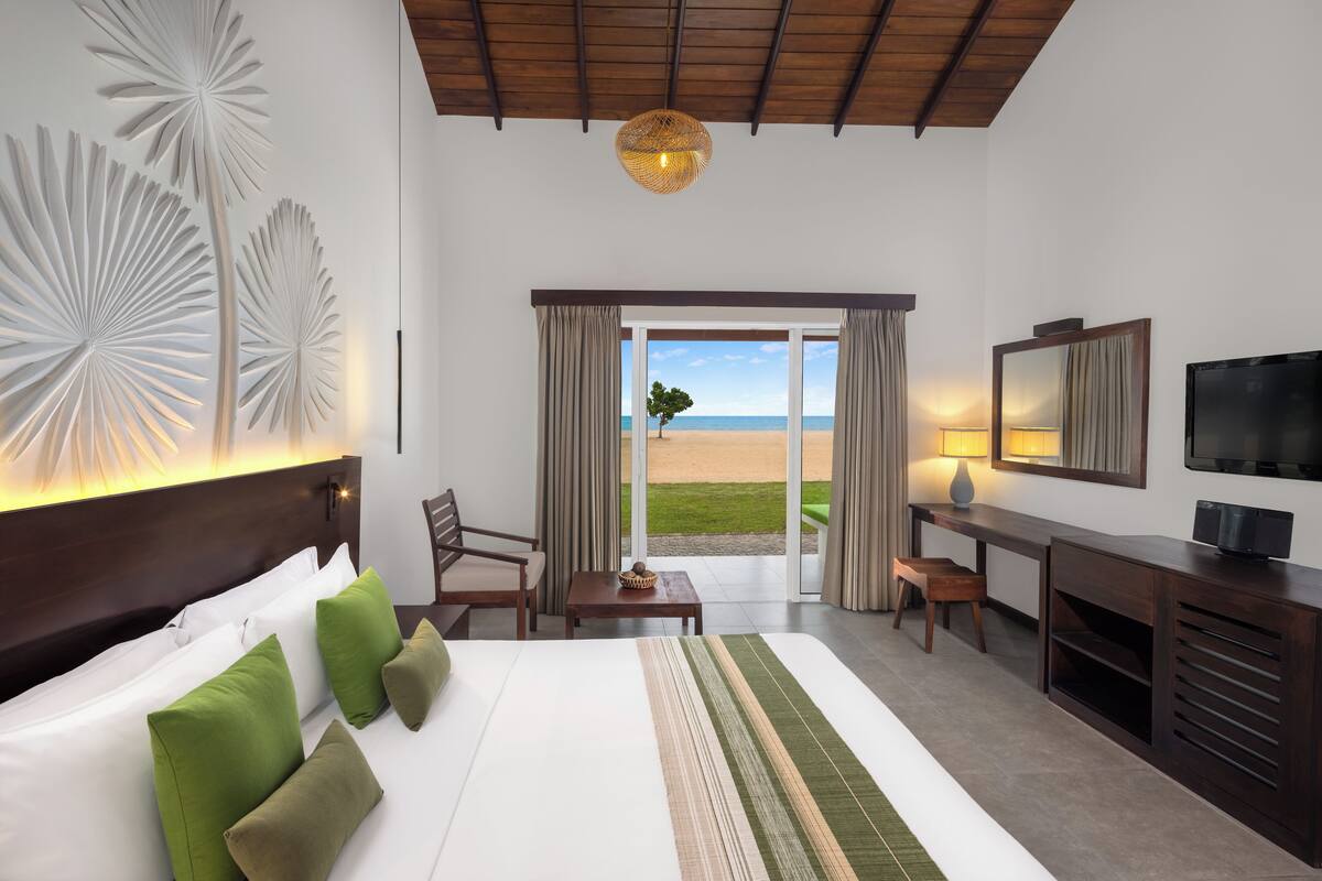 A hotel room with a large bed, a desk, a TV, and a view of the beach.