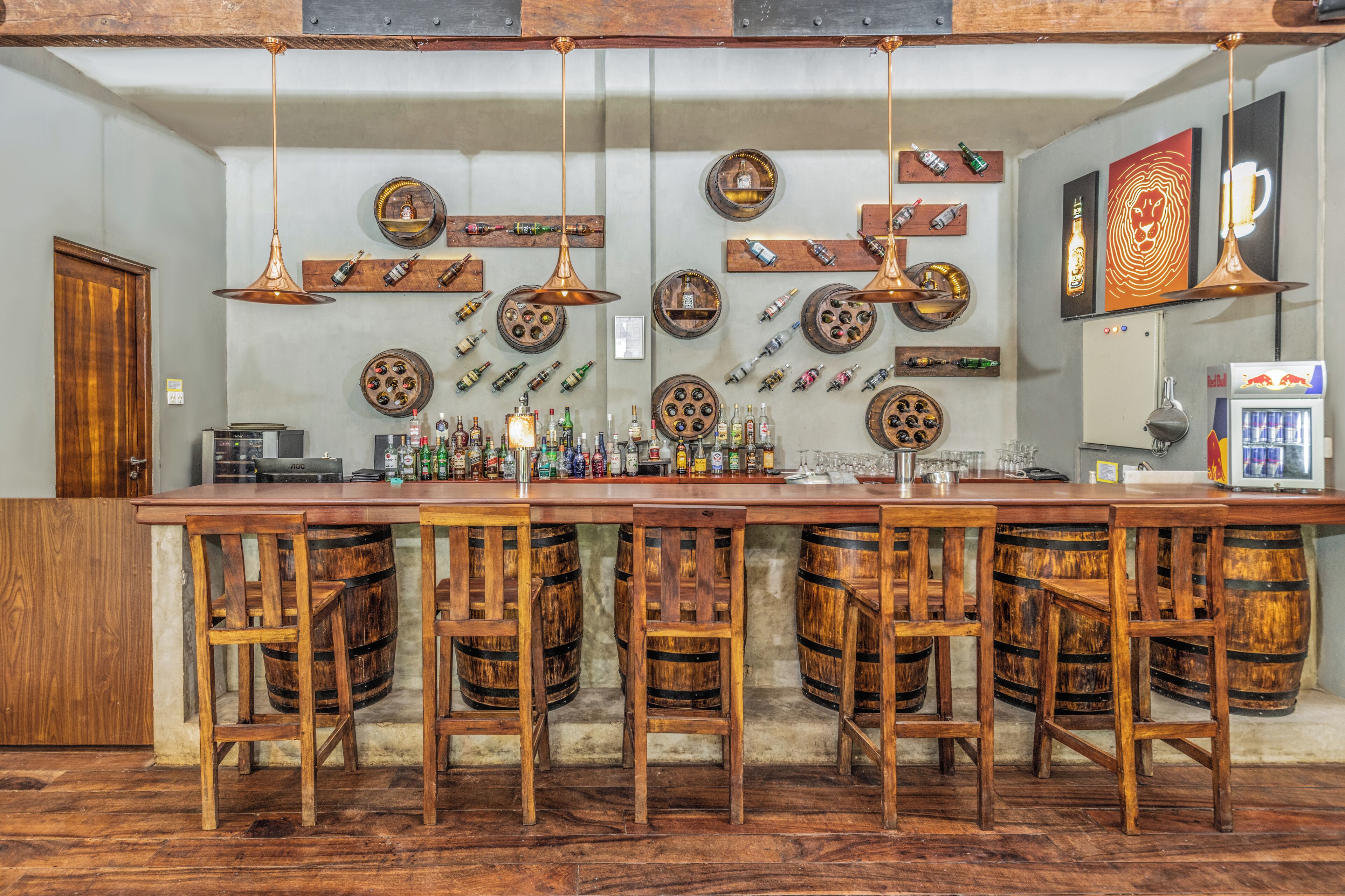 Un área de bar con taburetes de madera, una barra alargada y diversas botellas y vasos.