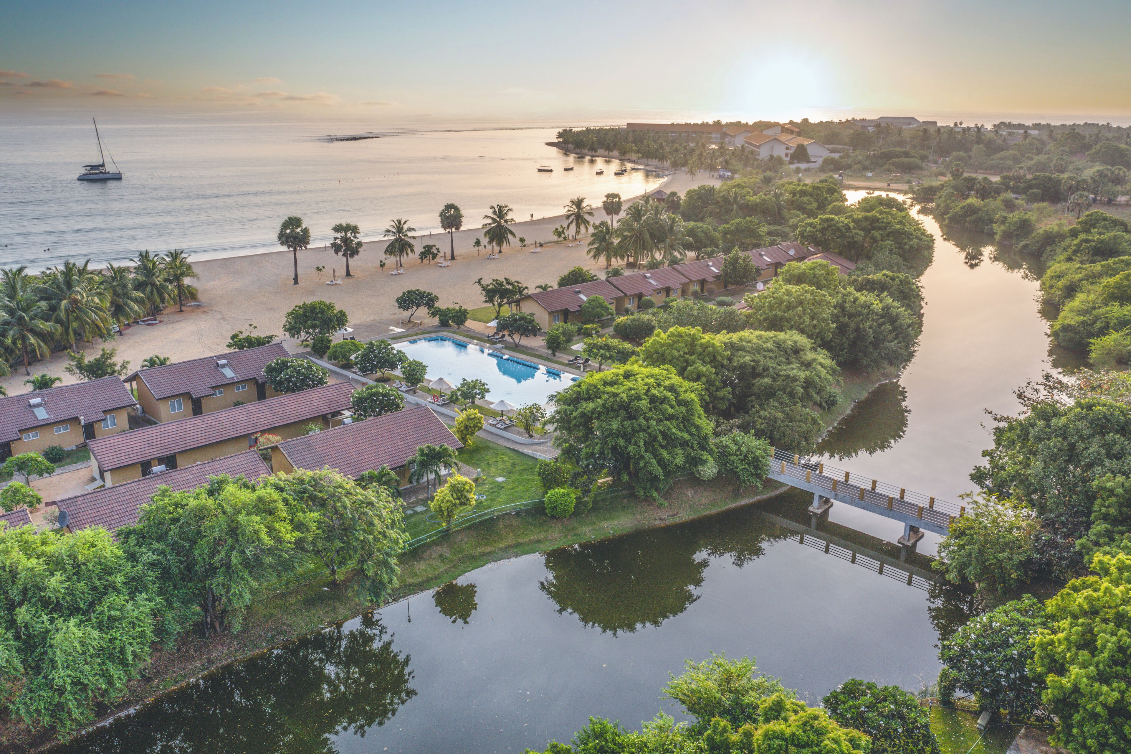 An aerial view of a resort with a swimming pool, beach, and a river.
