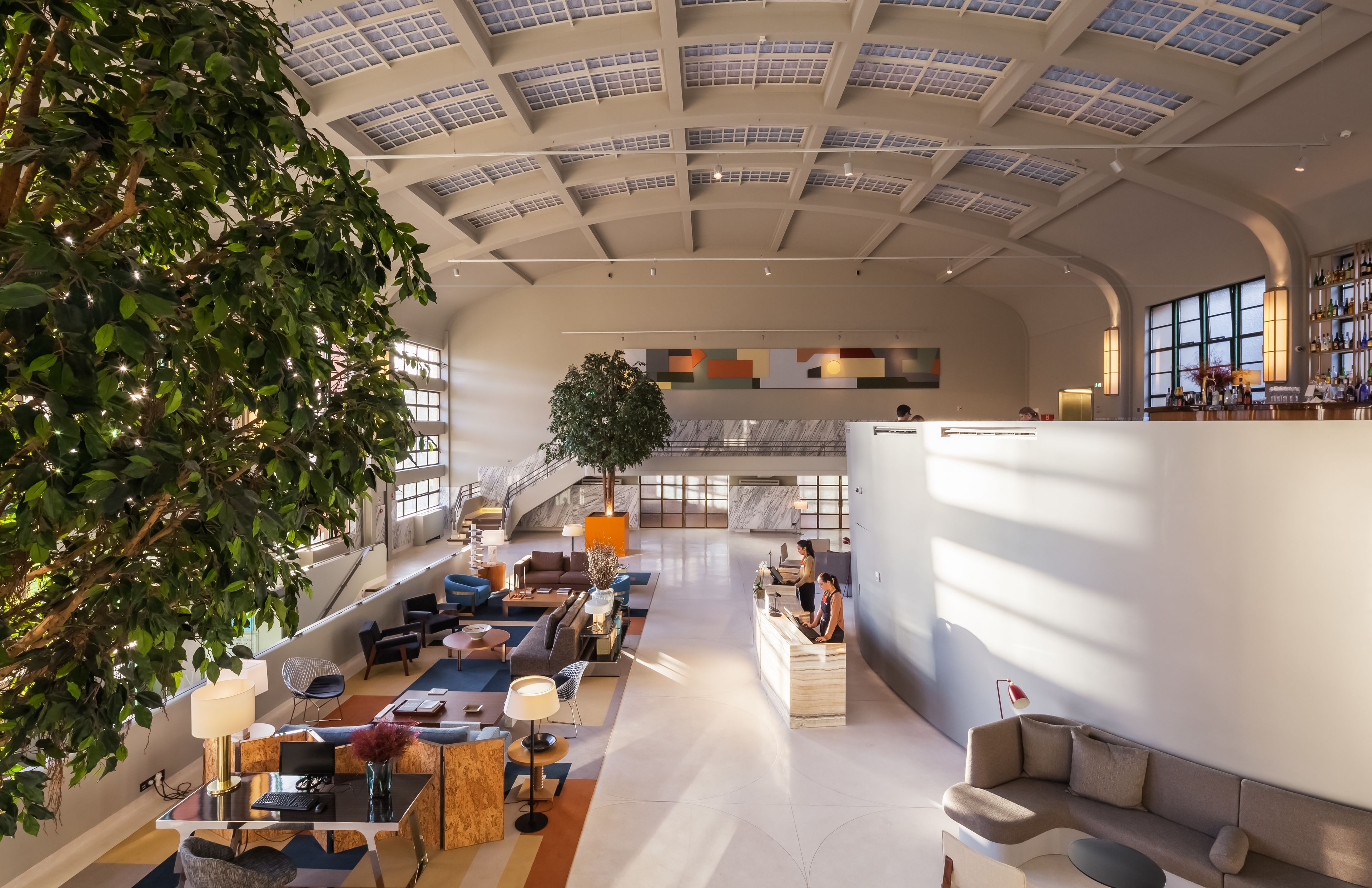 A spacious lobby with a high ceiling, a reception desk, seating areas, and a staircase leading to upper floors.