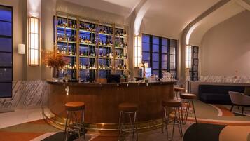 A bar area with a marble countertop, multiple stools, and a well-stocked shelf of bottles.