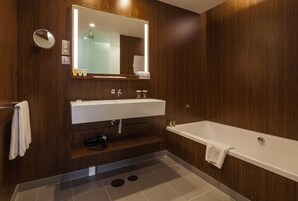 Uma casa de banho moderna com parede de madeira, um espelho grande, uma sanita branca, uma banheira e uma área de duche.