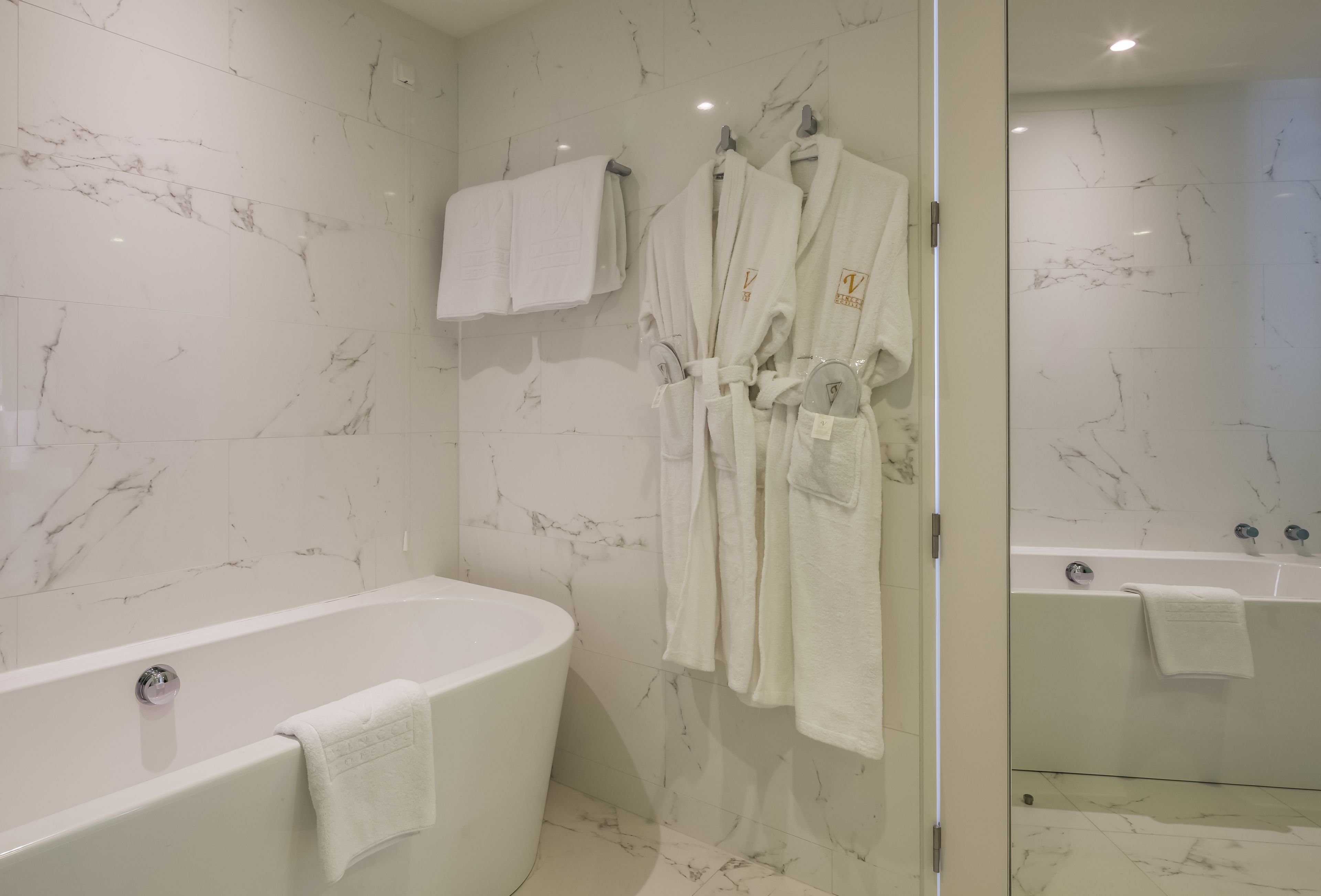 A modern bathroom with a freestanding bathtub, marble walls, and two white towels hanging on hooks.