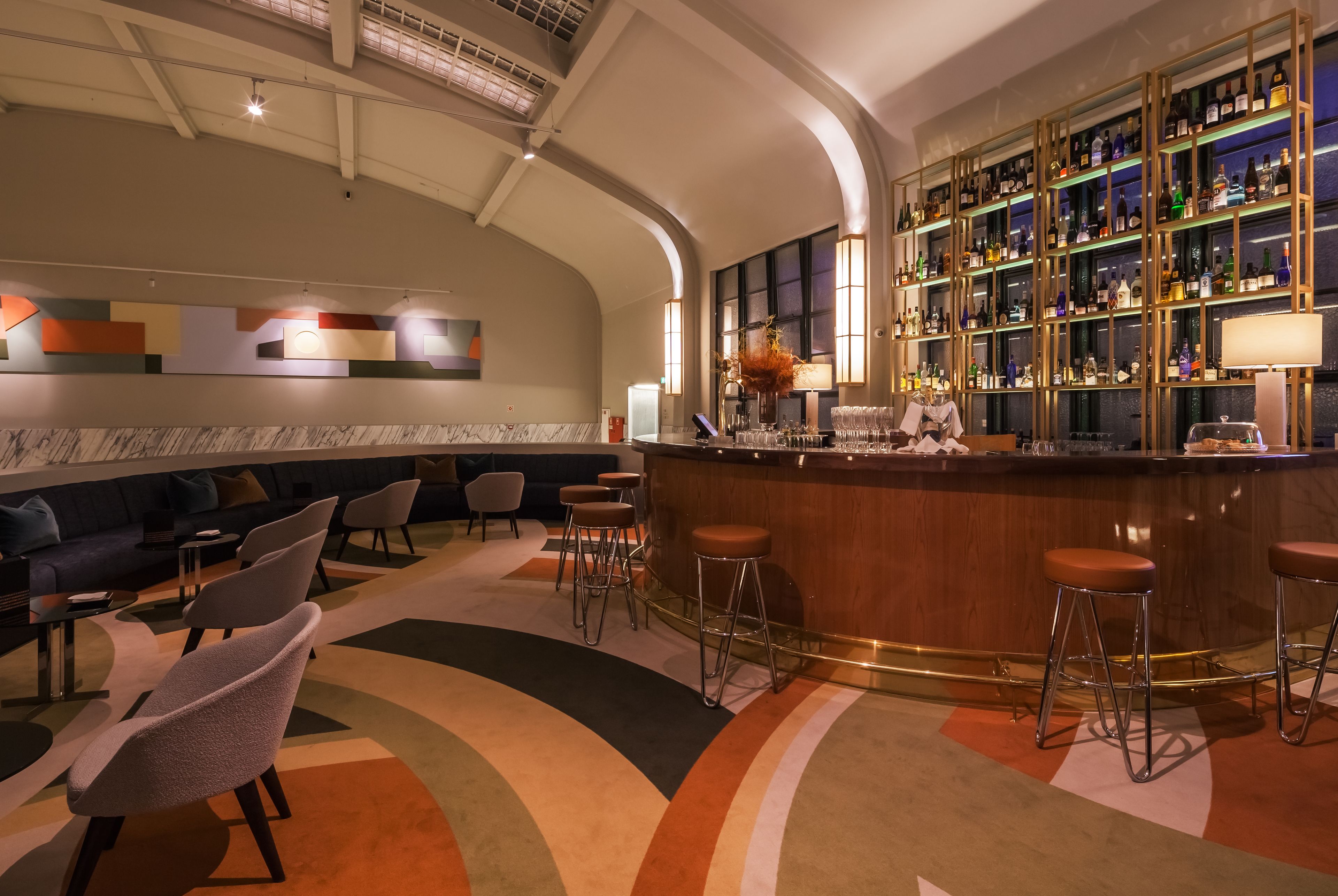 A bar area with a curved ceiling, a bar counter, stools, and a seating area with sofas and chairs.