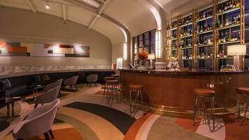 A bar area with a curved ceiling, a bar counter, stools, and a seating area with sofas and chairs.