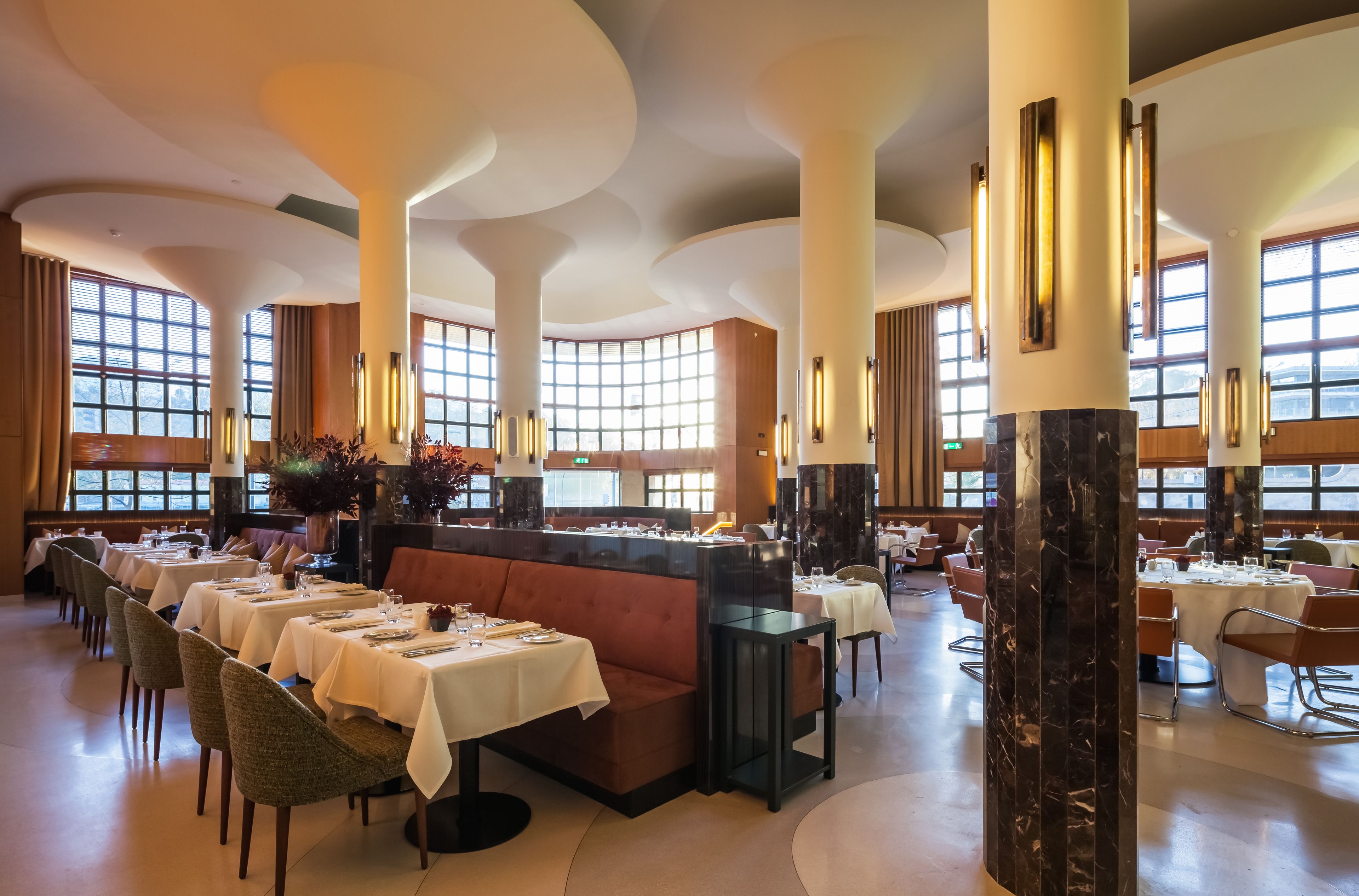 Uma ampla sala de jantar com pé direito alto, janelas grandes e luminárias modernas.
