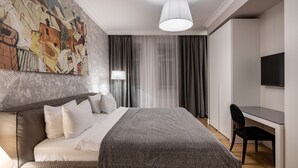 A modern hotel room with a large bed, a desk, a chair, a TV, and a painting on the wall.