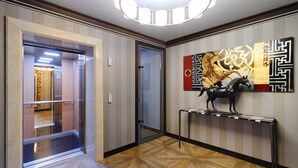 A modern hallway with a geometric patterned floor, a glass elevator, and a wall-mounted artwork featuring a horse.