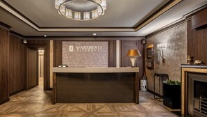 A reception area with a wooden reception desk, a chandelier, and a sign that reads "APARTMENTS CITYHOTEL".