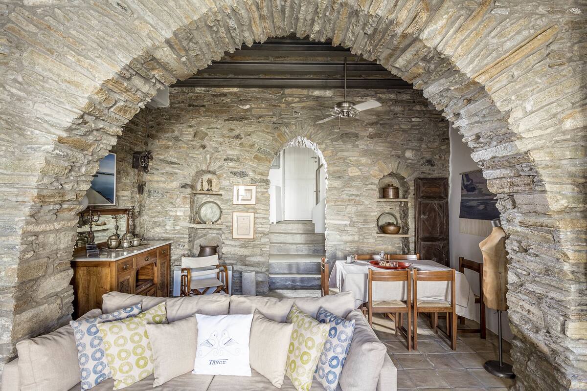 Una habitación con paredes de piedra, un sofá, una mesa de comedor y un ventilador de techo.