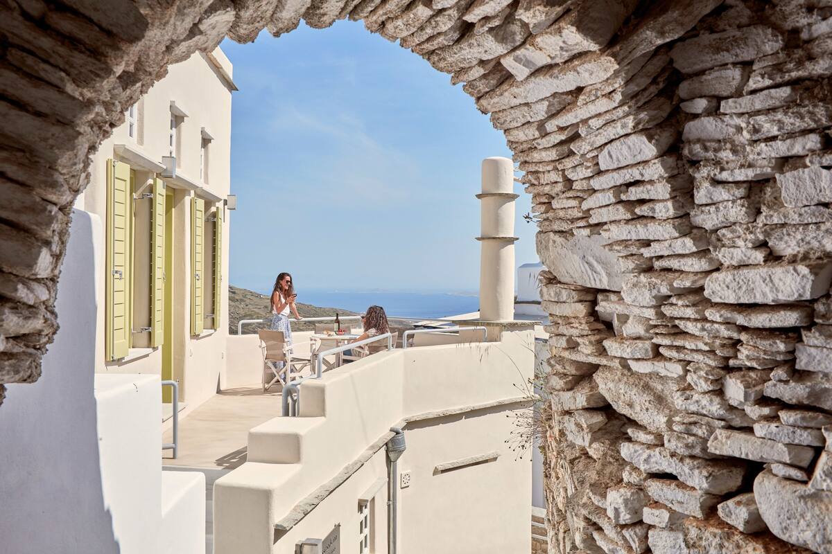 Un arco de piedra que conduce a una terraza con edificios blancos y vistas al mar.