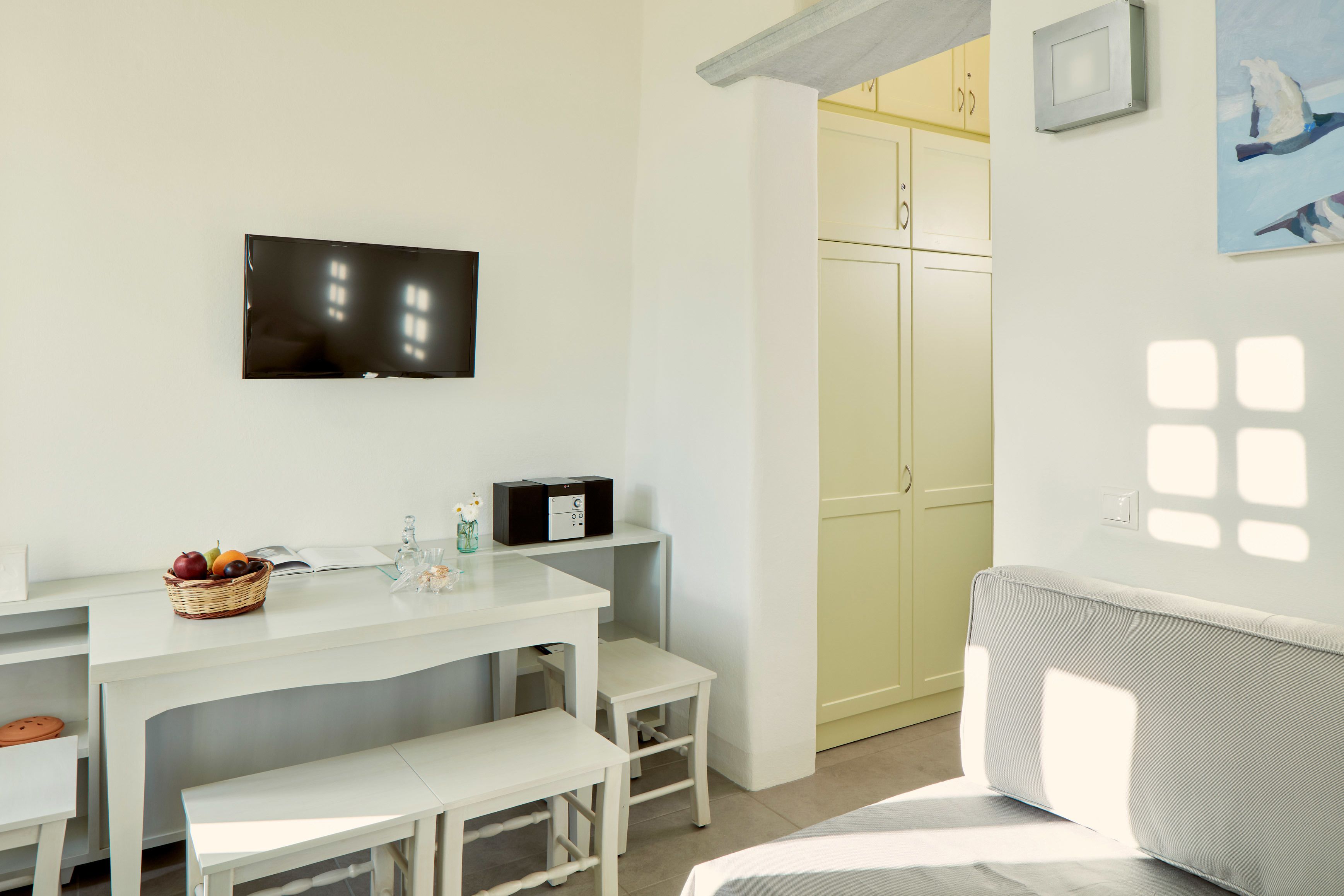A modern, well-lit room with a flat-screen TV, a small table with a fruit basket, a microwave, and a sofa.