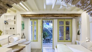 A bedroom with a bed, a small table, and a chair. There is a staircase leading to a balcony. - Crossroads Inn (Tinos)