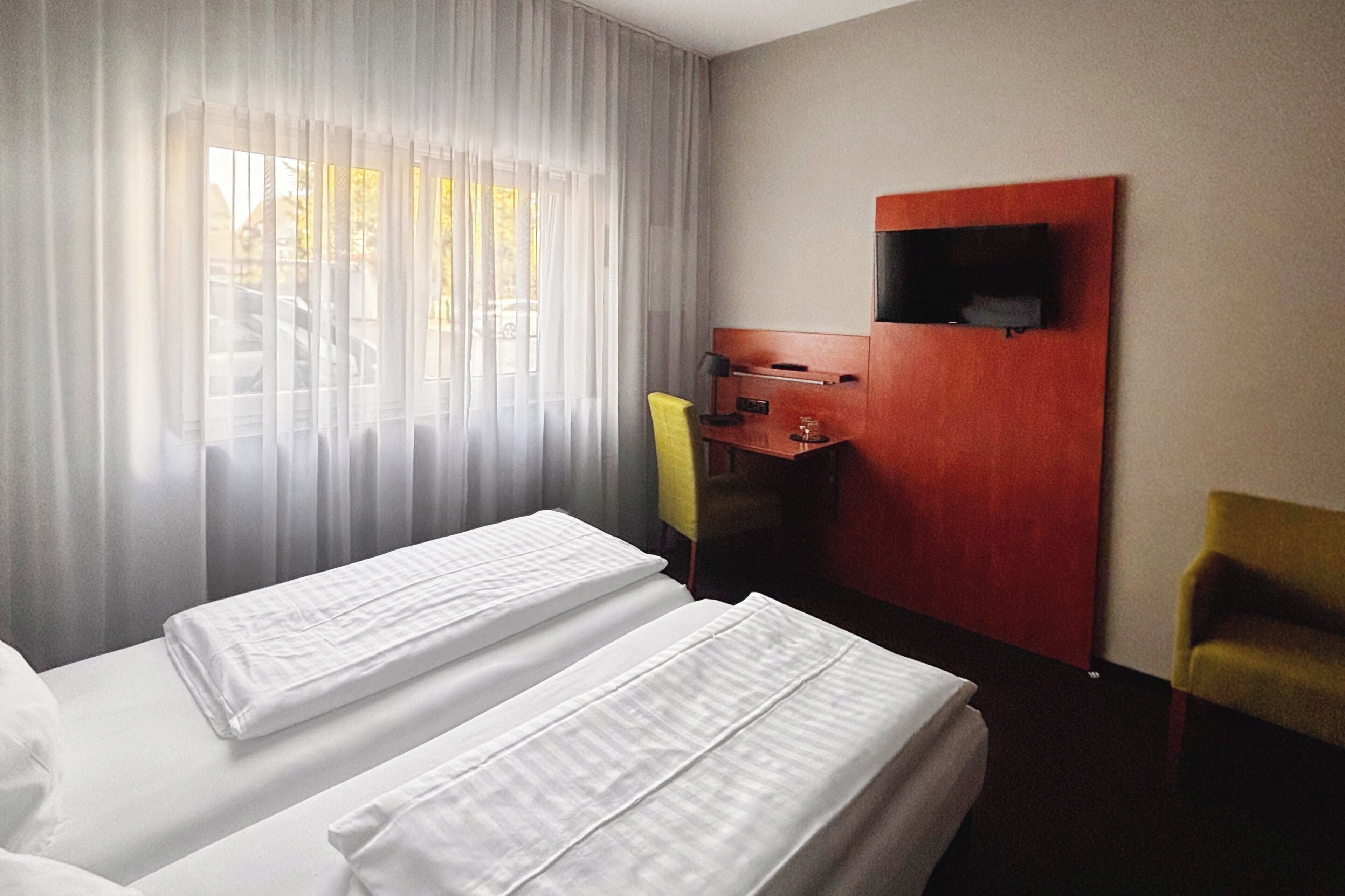 A hotel room with two beds, a desk, a chair, and a TV mounted on the wall.