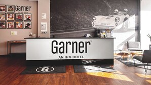 Zona de recepción de un hotel con el gran logotipo de Garner, un cartel de coche de carreras y una mesa de recepción.