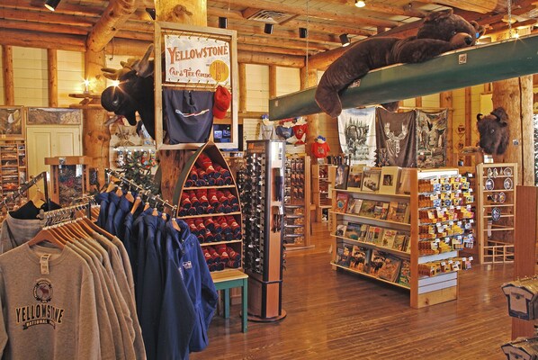 A store with wooden interiors, featuring clothing racks, a display of wine bottles, and various souvenirs.