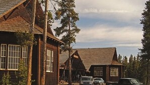 Un edificio rústico de madera con un porche, rodeado de árboles y vehículos estacionados.