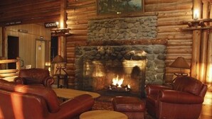 Interior de una cabaña de madera con chimenea de piedra, sofás de cuero y una mesita redonda.