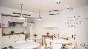 Una cucina moderna con mobili bianchi, un forno a microonde e un lavello. Ci sono sedie bianche attorno a un tavolo e una parete con una citazione motivazionale.