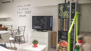 Un soggiorno moderno con una TV a schermo piatto, una macchina da caffè e un'area pranzo con sedie e tavolo.