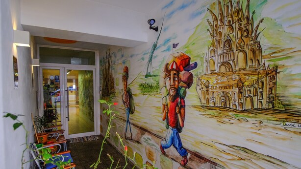Un murale raffigura un castello e due figure, un portone con pannelli di vetro e una telecamera di sicurezza.