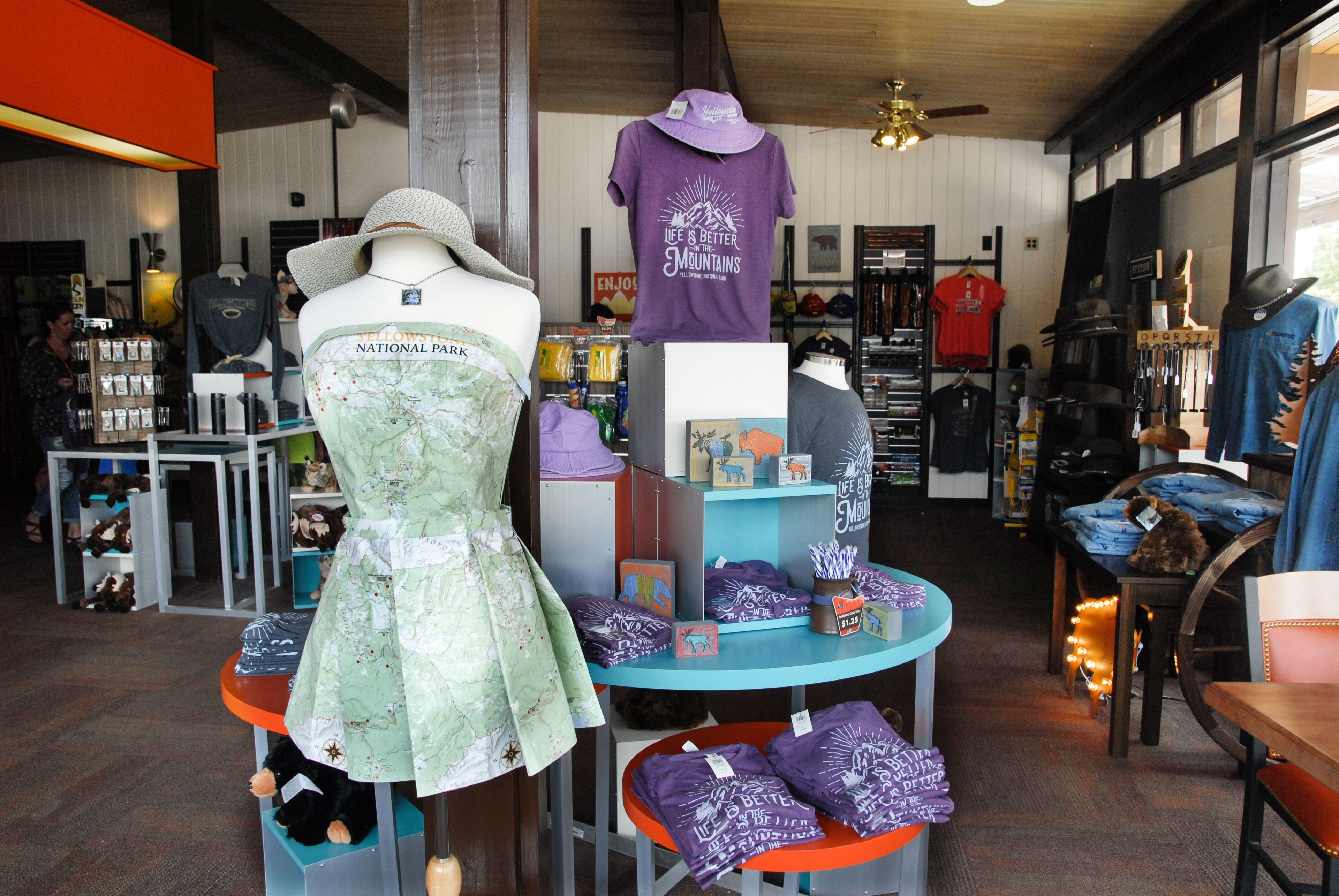A retail store with various clothing items, including a mannequin in a green dress, a purple t-shirt, and hats.