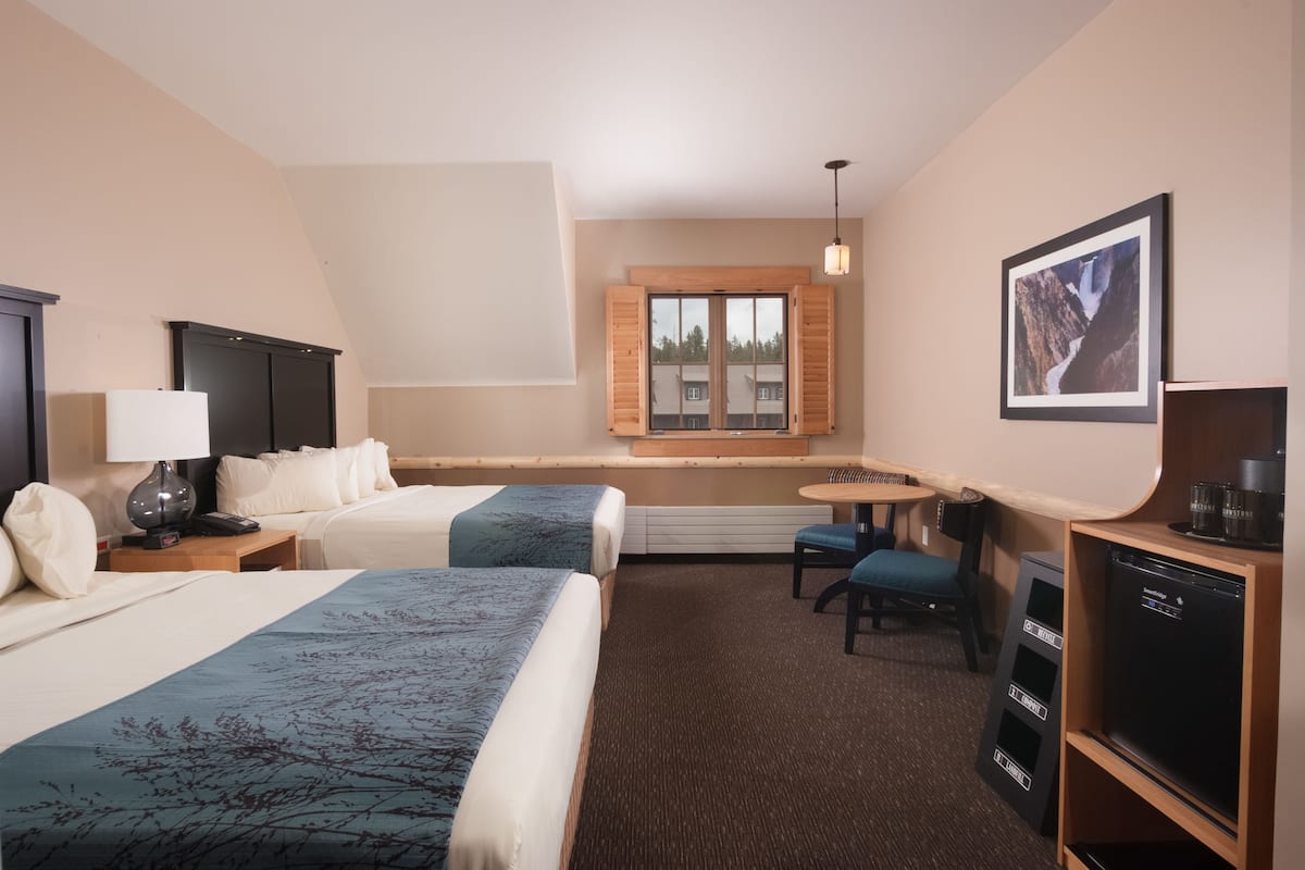 Ett hotellrum med två sängar, ett skrivbord, en stol, en tv och ett fönster med utsikt över byggnader.