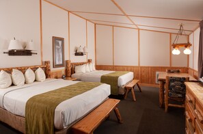 A room with two beds, wooden headboards, a bench, a table, and wall-mounted lamps.