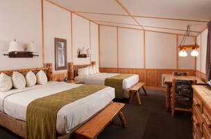 Habitación con dos camas, cabeceros de madera, un banco, una mesa y lámparas fijadas a la pared.